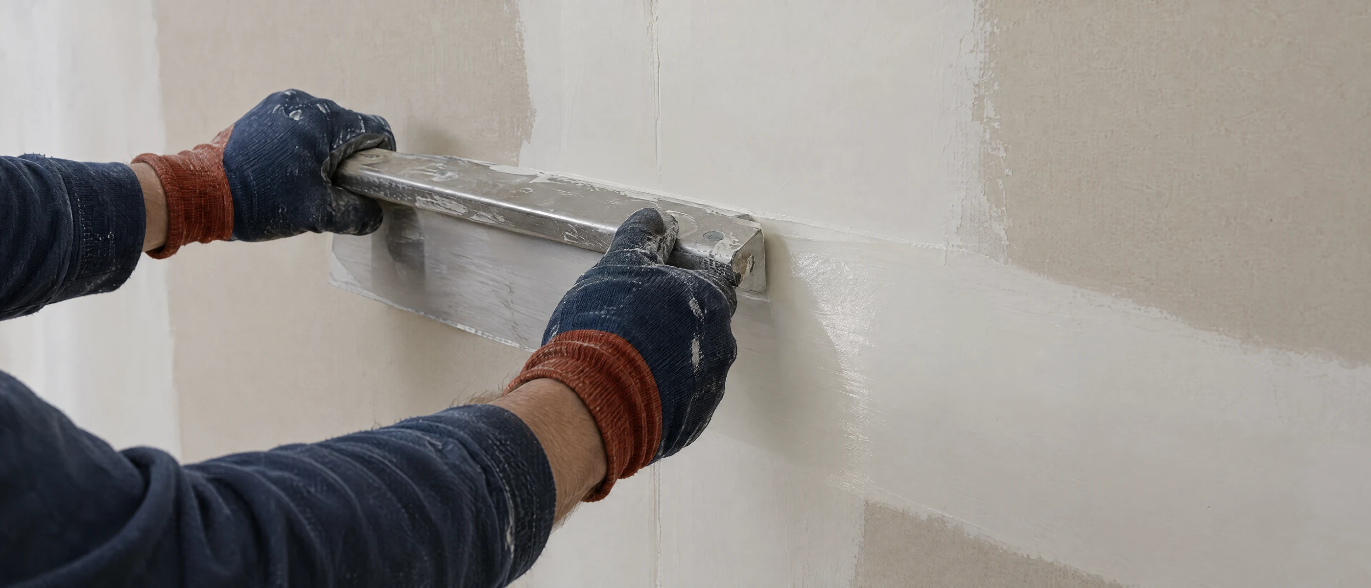 Hände spachteln eine Gipskartonwand